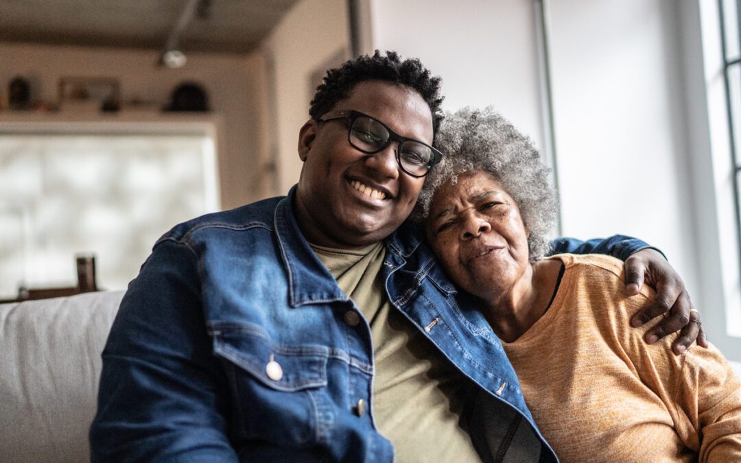 Adult child sitting on couch with arm around elderly mother suffering from cognitive impairment