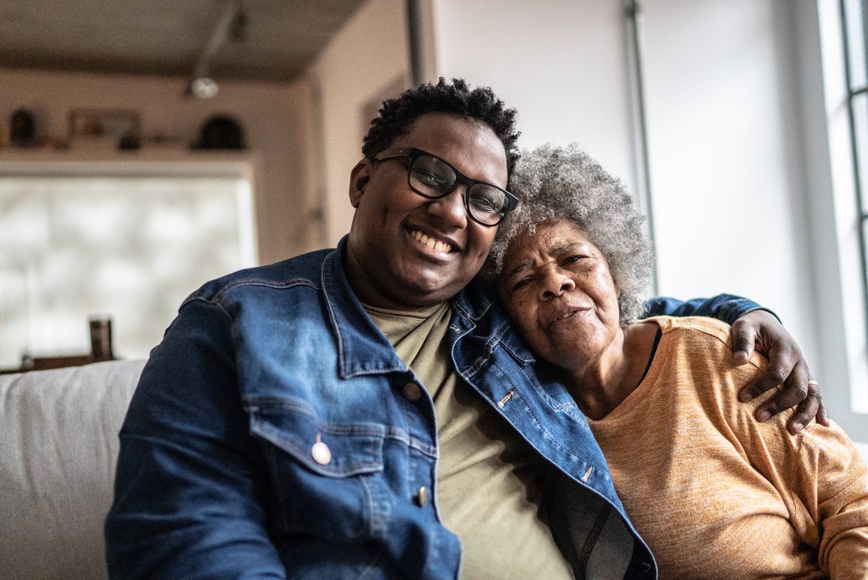 Adult child sitting on couch with arm around elderly mother suffering from cognitive impairment