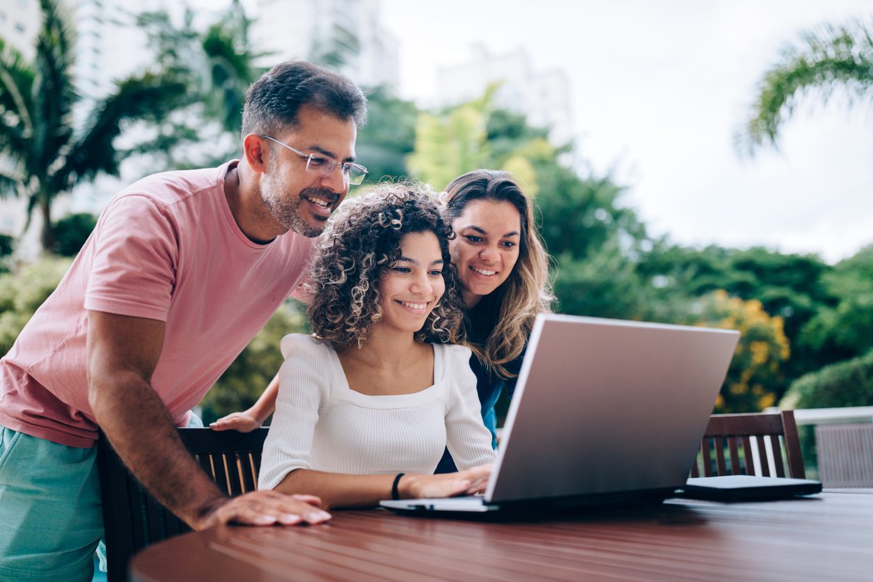 Parents sitting outside with teenage daughter on laptop discussing her custodial Roth IRA