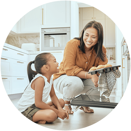 Mom taking muffins out of oven with young daughter watching representing planned ahead financial planning clients