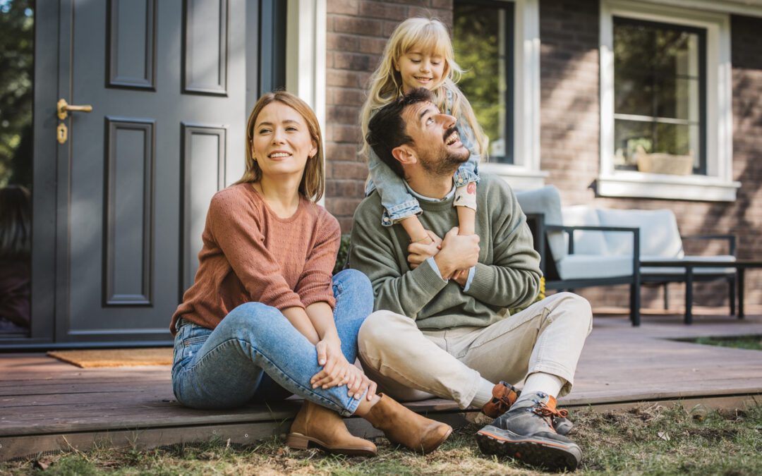 Mother and father on front porch step with young daughter hugging dad from behind