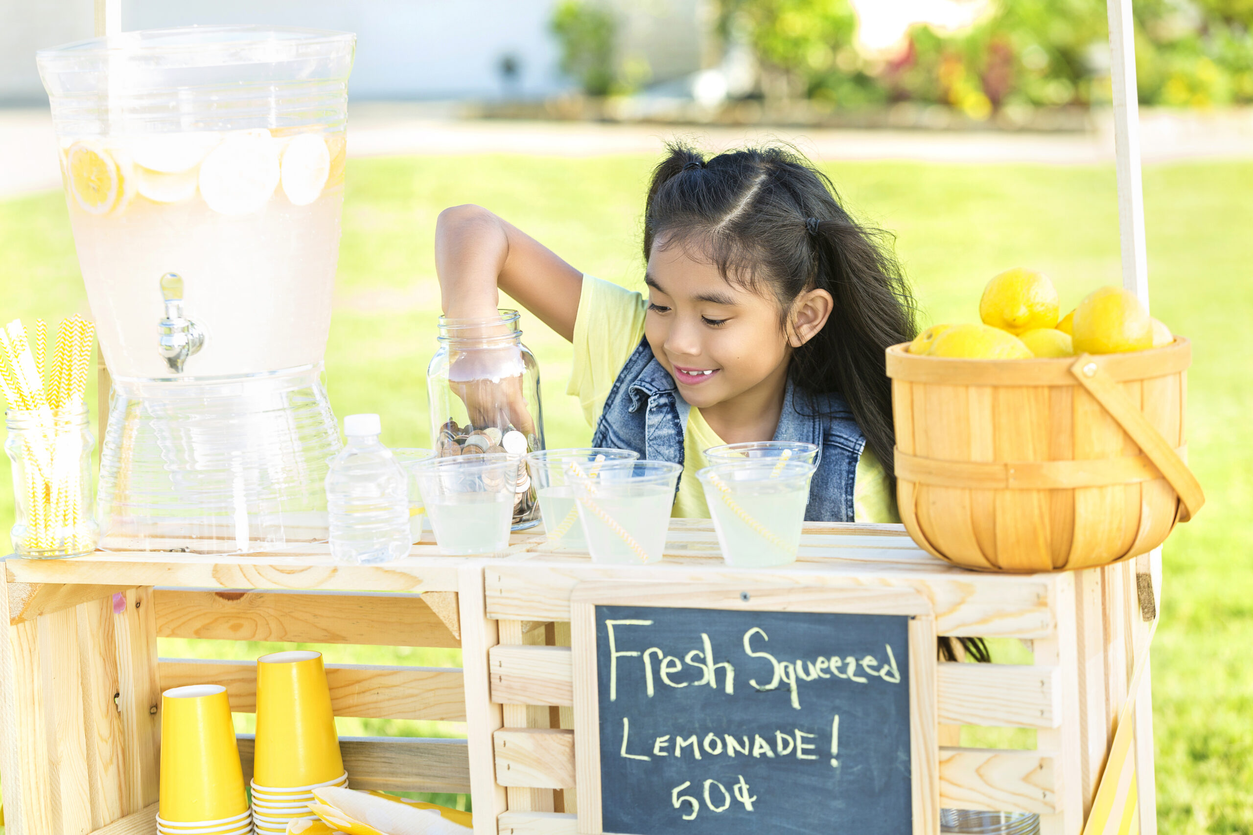 Little girl learning about money with her hand in money jar at her lemonade stand